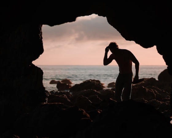 Un homme se tient devant l'ouverture d'une grotte à contrejour.